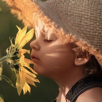 Enfant avec un chapeau de paille renifle de près un tournesol