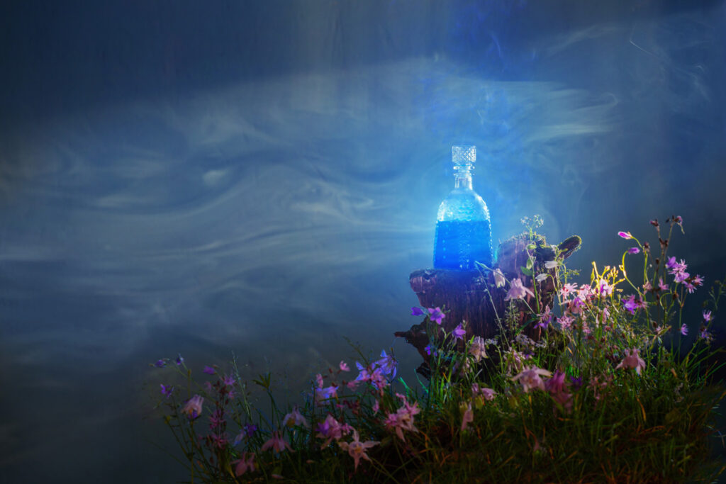 Visuel affichant un Elixir bleu illuminé posé au centre d'une atmosphère mystique fleurie et embrumée pour Terre de Rêves dans l'Ain